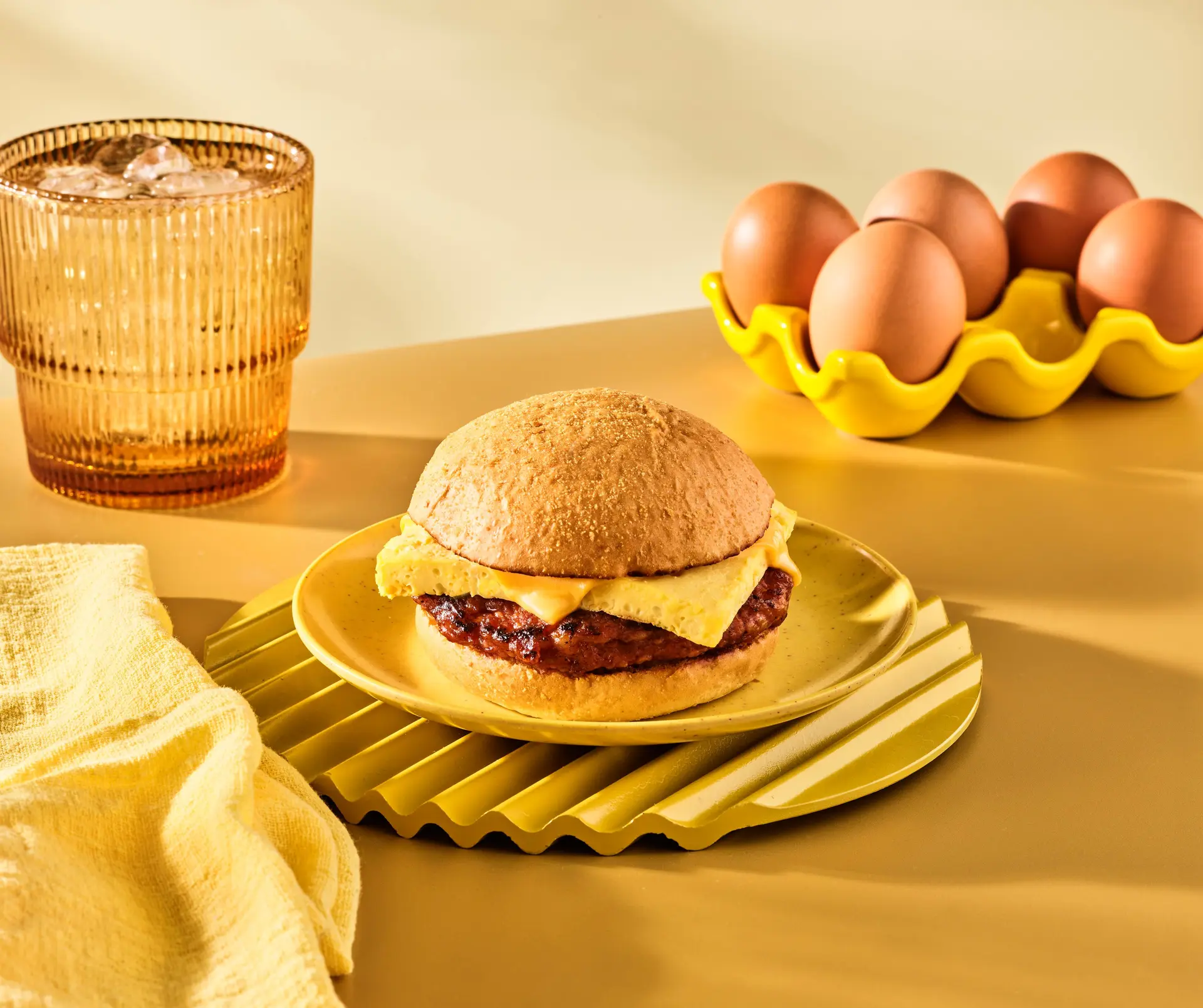 Longanisa Breakfast Sandwich on a plate in front of a glass of water and eggs, with a yellow background.