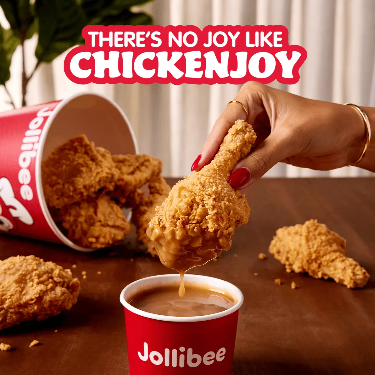 A bucket of fried chicken tipped over and a hand holding a drumstick dipped in gravy with 'There's no joy like Chickenjoy' text.